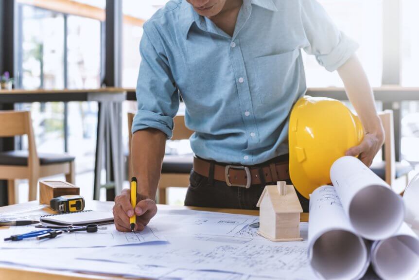 A contractor wearing a blue shirt writing on house plans.